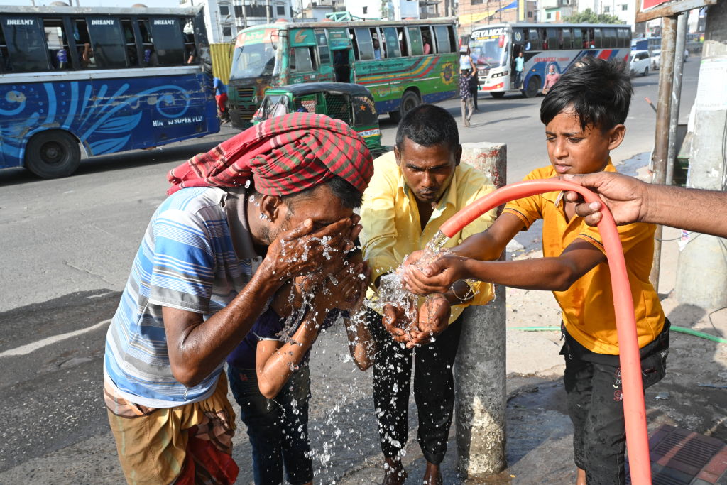 Three people drink water and wash their faces to try to cool off during a heat wave in Bangaldesh. 