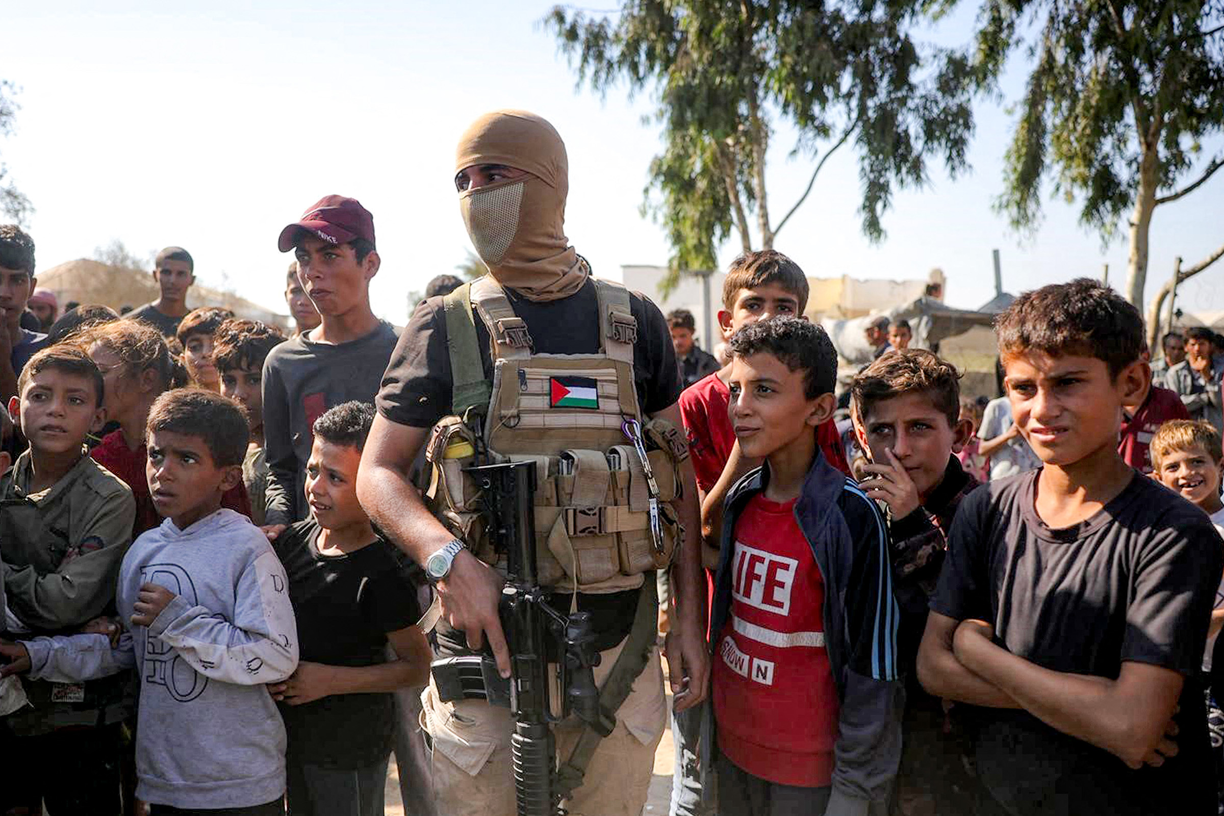 Seorang pejuang militan Palestin bertopeng dari Briged Ezzedine al-Qassam, sayap bersenjata gerakan Hamas Palestin, berdiri mengawal di sebelah kanak-kanak sebelum ketibaan kenderaan Jawatankuasa Antarabangsa Palang Merah (ICRC) di selatan Deir el-Balah di tengah Semenanjung Gaza.